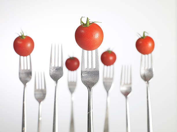 close up view of a fresh cherry tomato on fork isolated on a black background.