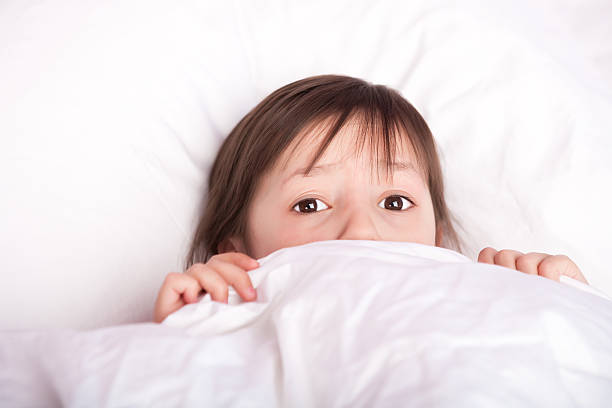 Scared cute 4 years old girl laying under duvet