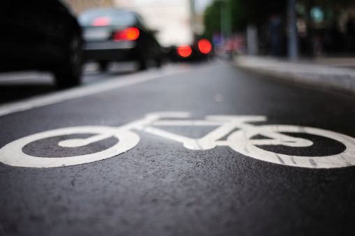 Bike lane on a rainy day. Sign for bicycle painted on the asphalt. Car and traffic in background. Dividing line, diminishing perspective. See also:
