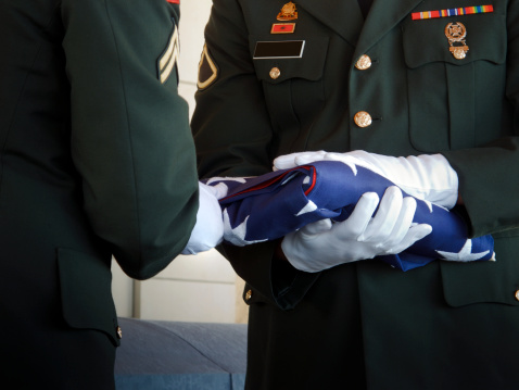 This military honor guard carefully folds the United States flag for presentation to family members at a veteran's funeral. Selective focus on flag and gloved hands. Would make good illustration for U.S. Veteran's Day, U.S. Memorial Day or honoring military service.