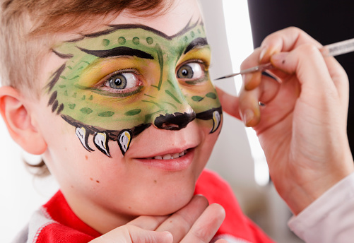 A portrait of a young boy having a mask painted onto his face.