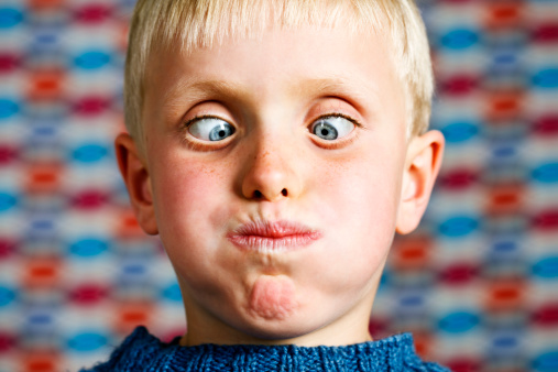 This cute blond 7 year old boy is really having fun, crossing his eyes and blowing out his cheeks as he looks down at his possibly very full mouth! Shot with Canon EOS 1Ds Mark III.