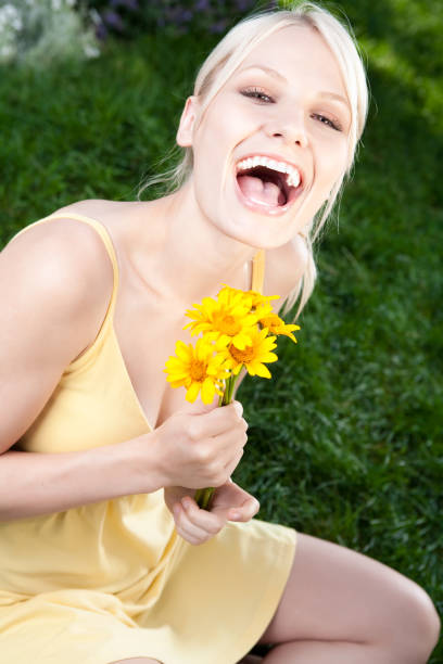 A happy young woman covering eyes with fresh pink Gerber Daisy flowers, isolated on white