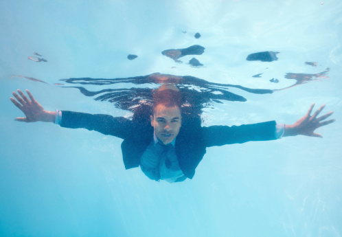 Portrait of a male business executive in full suit swimming under water in pool