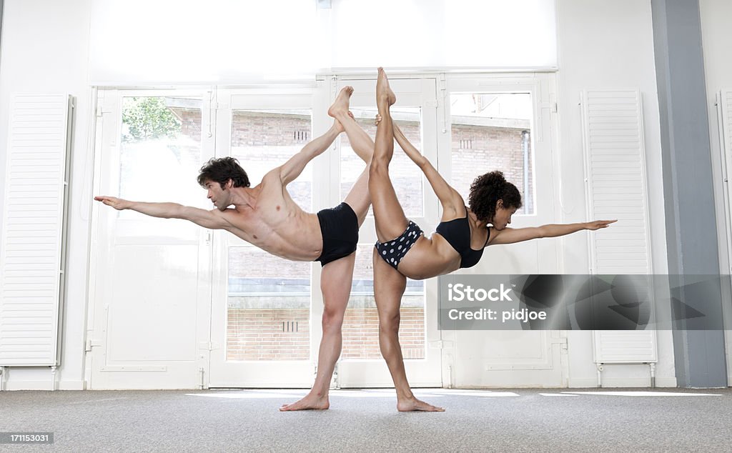 man and woman performing standing bow pulling pose XXXL image man and woman in sports clothing performing standing one legged upward facing bow pose in yoga studio Men Stock Photo