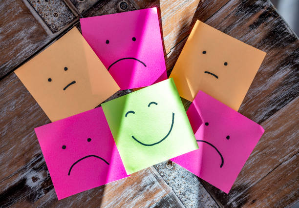 Top view of different emotions expressed with black ink on sticky notes scattered on marble surface while green cheerful sticker placed on top of sad and depressed feelings in sunlight