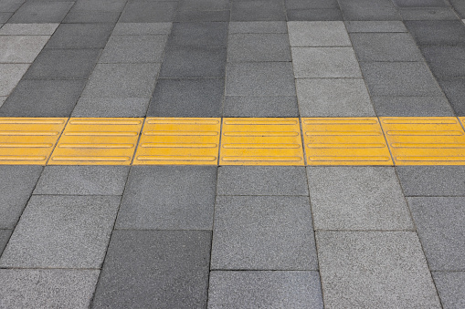 Yellow tactile tiles are installed on outdoor pedestrian walkways to provide tactile ground surface indicators, aiding individuals who are blind or visually impaired. These detectable warnings are designed to assist outside.