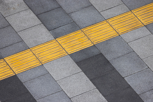 yellow tactile tiles are installed on outdoor pedestrian walkways to provide tactile ground surface indicators, aiding individuals who are blind or visually impaired. These detectable warnings are designed to assist outside.