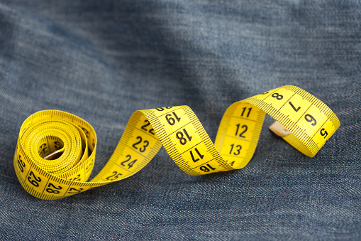 Yellow measure tape on jeans material