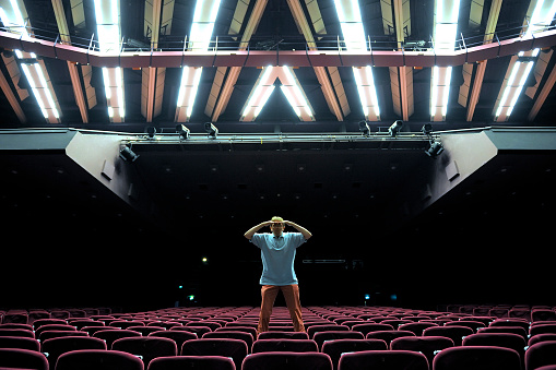 man standing on red velvet seat in empty auditorium looking at the camera with two hands above his eyes, iStockalypse Cannes 2010 