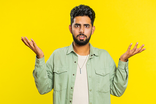 What. Why. Angry Indian man raising hands in indignant expression, asking reason of failure, demonstrating disbelief irritation by troubles. Arabian young guy isolated on yellow studio background