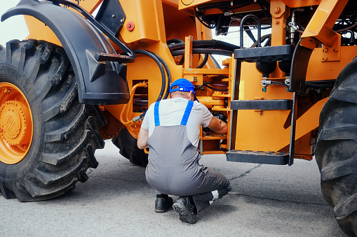 Professional mechanic repairs wheeled tractor or bulldozer. Workshop and maintenance service for agricultural machinery. Truck repair and diagnostics.