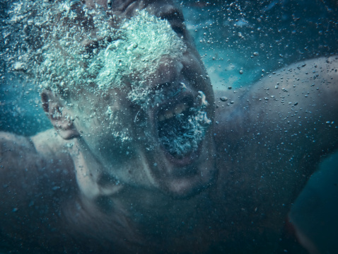 Man drowning, screaming underwater. Focus on air bubbles