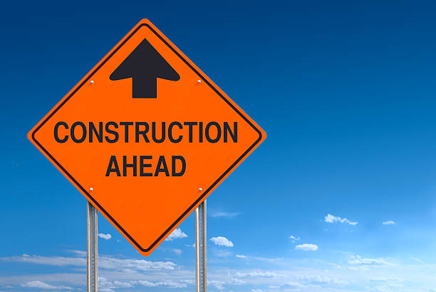 оранжевый предупреждения, строительство впереди сообщение дорожный знак над голубое небо - road sign road construction sign construction стоковые фото и изображения