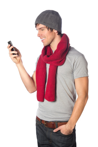 A young guy wearing casual winter accessories looks at his smart phone.
