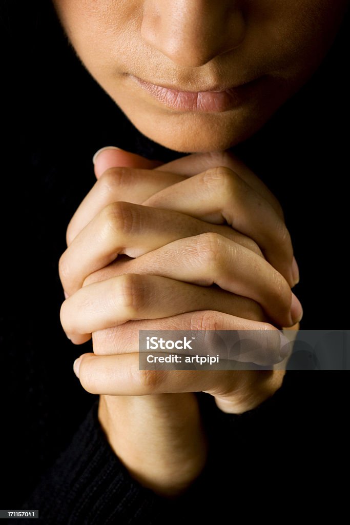 Woman praying with hands closed in the dark close-up of young woman praying, black background Forgiveness Stock Photo