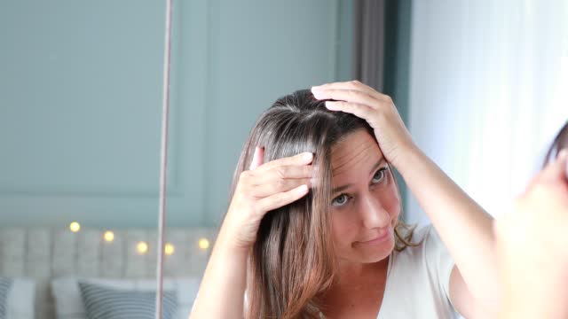Young woman looking in mirror and having problem with hair loss