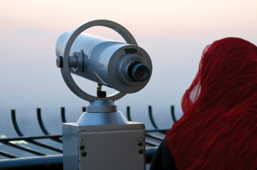 An anonymous Muslim woman standing behind a monocular atop the Cairo Tower in Egypt.