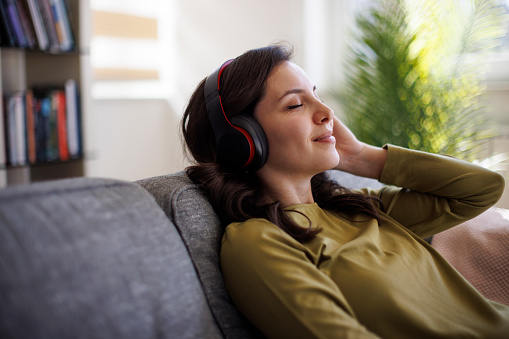 Young smiling woman with bluetooth headphones relaxing on sofa