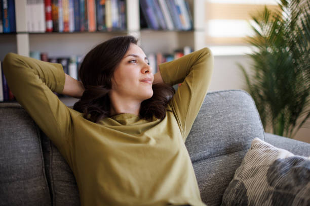 Happy thoughtful smiling woman relaxing on sofa at home stock photo