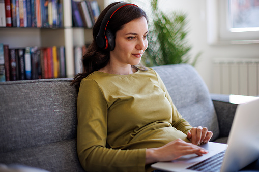 Young smiling woman with headphones sitting on sofa and using laptop