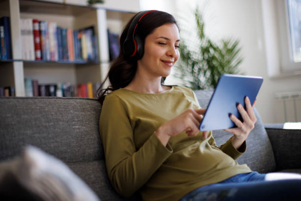 улыбающаяся расслабленная женщина отдыхает на диване с помощью цифрового планшета - digital tablet audio стоковые фото и изображения