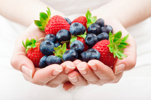 Woman holding a handful of fresh blueberries and strawberries. Horizontal framing, shallow depth of field used.