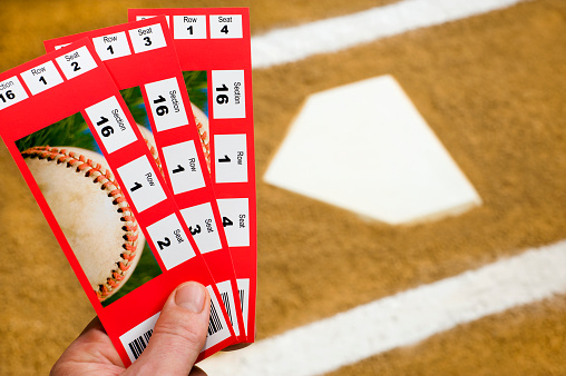 A Hand holding three baseball ticket stubs at home plate with the chalk lines of the batter's box