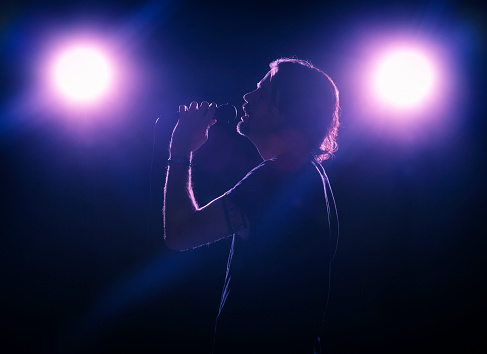 A silhouetted man singing with stage lights in the background. Photographed directly into the lights to create flare. Noise added to enhance simulated concert effect.
