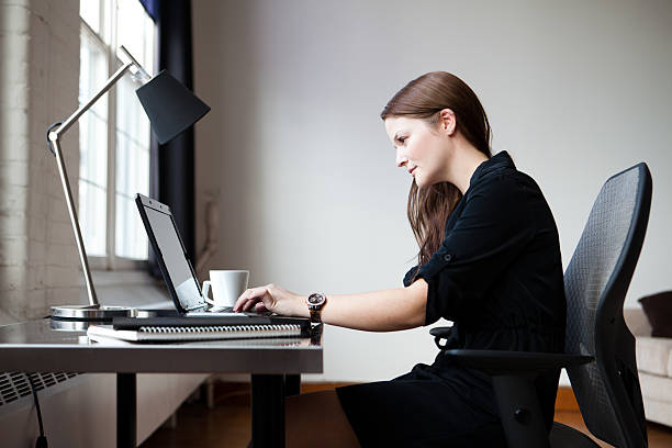 Young businesswoman in an office A young businesswoman in an office working on a laptop computer. desk lamp photos stock pictures, royalty-free photos & images