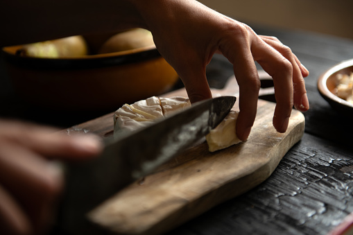 Woman hand cutting Camembert on wooden board