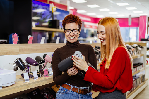 Beautiful LGBT couple buying home appliances in electronic store or shop. They are choosing and buying hairdryer and personal hygiene equipment.