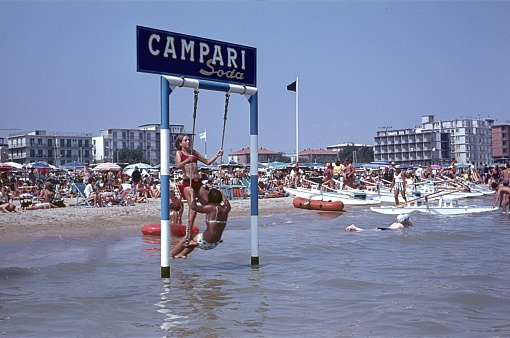 Rivazzurra, Rimini Region, Emilia Romagna, Italy, 1966. Holidaymakers from Italy and Central Europe cavort on the beach at Rivazzurra. Furthermore: the well-known Camparie swing, hotels, boats and parasols.