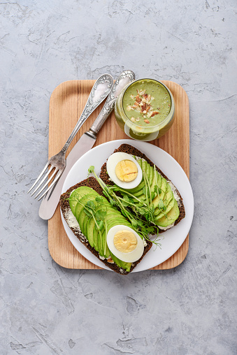 Avocado Sandwich with boiled Egg - sliced avocado and egg on rye toasted bread for healthy breakfast or snack on wooden tray, top view