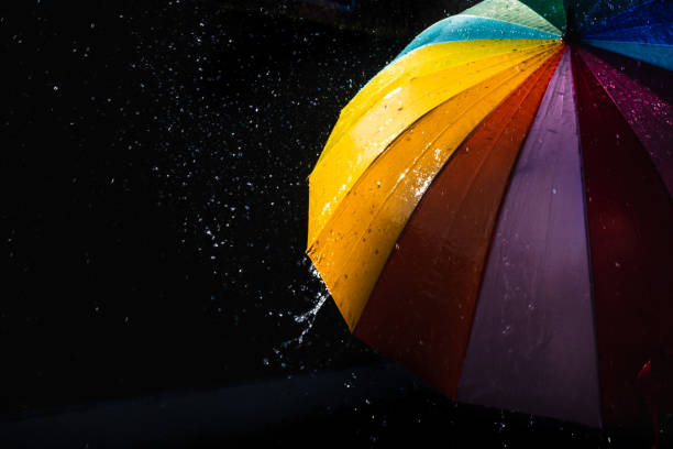 istock Rain on a warm-toned umbrella lit by the sun, isolated on black background with copy space. 1711783060