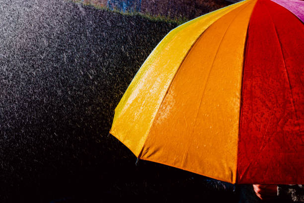 istock Rain falls on an umbrella among sun rays, dark background in black. 1711783085