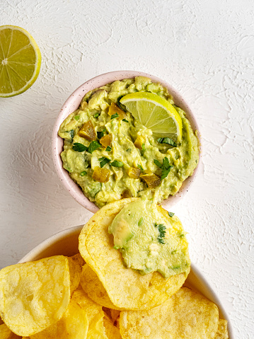 Mexican guacamole with nacho chip in wooden bowl on rustic wooden table. Top view. Traditional mexican food