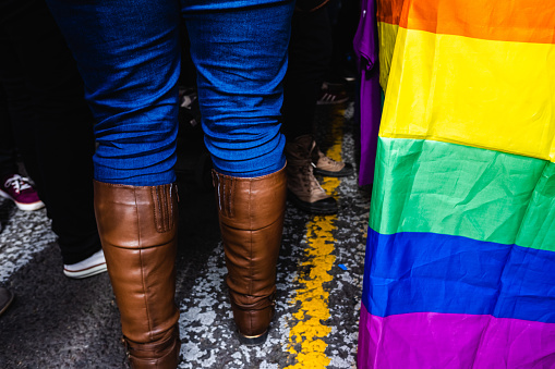 Legs of women walking in an LGBT demonstration between rainbow flags.