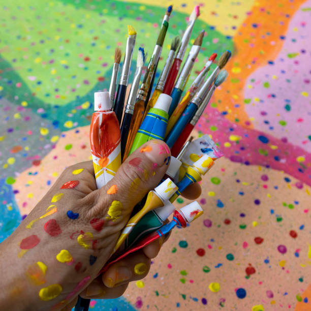 istock Hand holding paint tubes and paintbrushes 1711805560