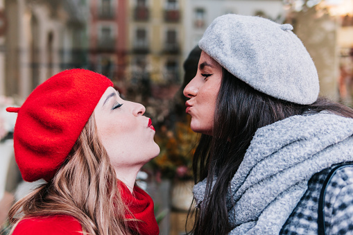Close-up profile of two female friends blowing a kiss to each other in the street