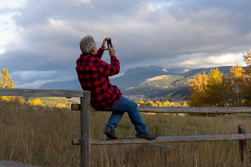 He uses mobile phone, mountains and sun rise in distance, Crowsnest Pass, Alberta