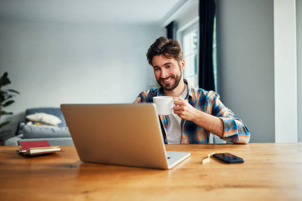 istock Happy man working with laptop at home sitting at a table drinking from a cup 1711836727