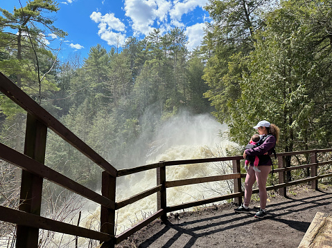 Mother with baby in sling looks at waterfall on trail