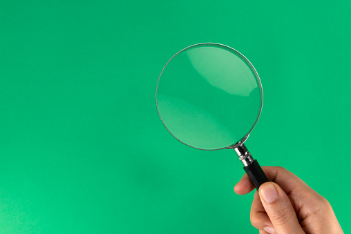 Holding magnifying glass, green background.