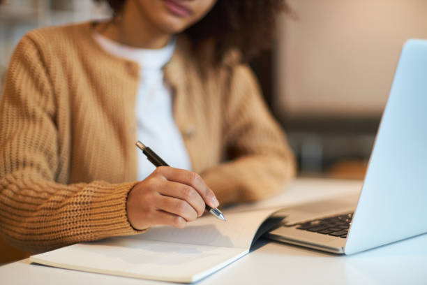 istock Close-up of female hand holding a pen and making notes on notepad while telecommuting on laptop 1711858879