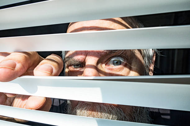 Close-Up Senior Man Staring Through Window Blinds Fearfully