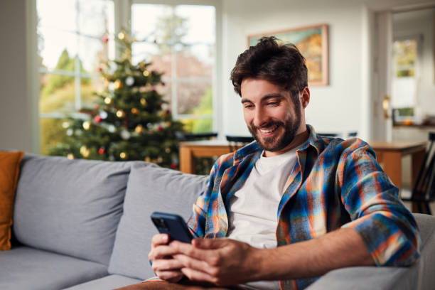 istock Happy young man sitting on the sofa using mobile phone during Christmas time at home 1711875643