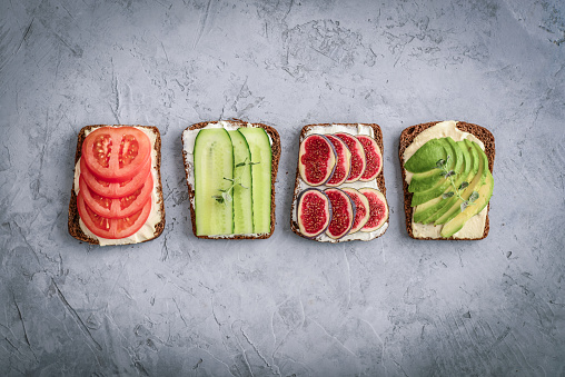 Vegetarian sandwich with cucumber, tomato, figs and avocado on rye bread on grey background, top view