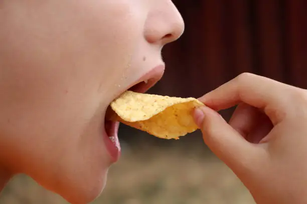 A teenager eats a chips. Close-up photo of a mouth without eyes.