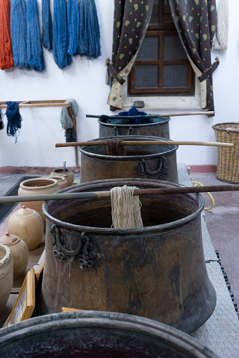 selective focus os a pots for the handmade dyeing of wool or silk, with pots with natural products for dyeing, and skeins of wool already dyed hanging on the wall, vertical